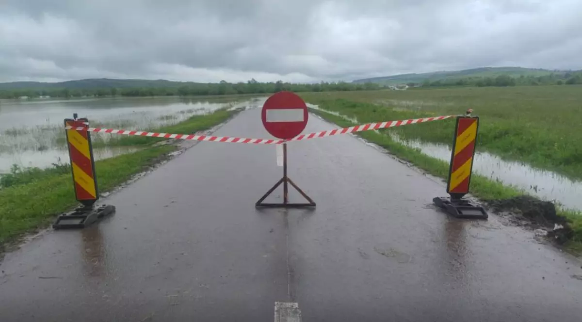 Imaginea surprinde un drum județean complet închis circulației, marcat cu bandă de interdicție și semn de acces interzis, din cauza inundațiilor.