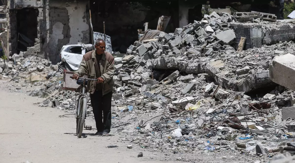 Poză cu un bărbat care ține de coarne o bicicletă în timp ce trece pe lângă dărâmături, în Fâșia Gaza