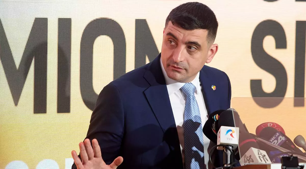 George Simion, îmbrăcat într-un costum bleumarin, cămașă albă și cravată albastră, în timpul unei conferințe de presă.