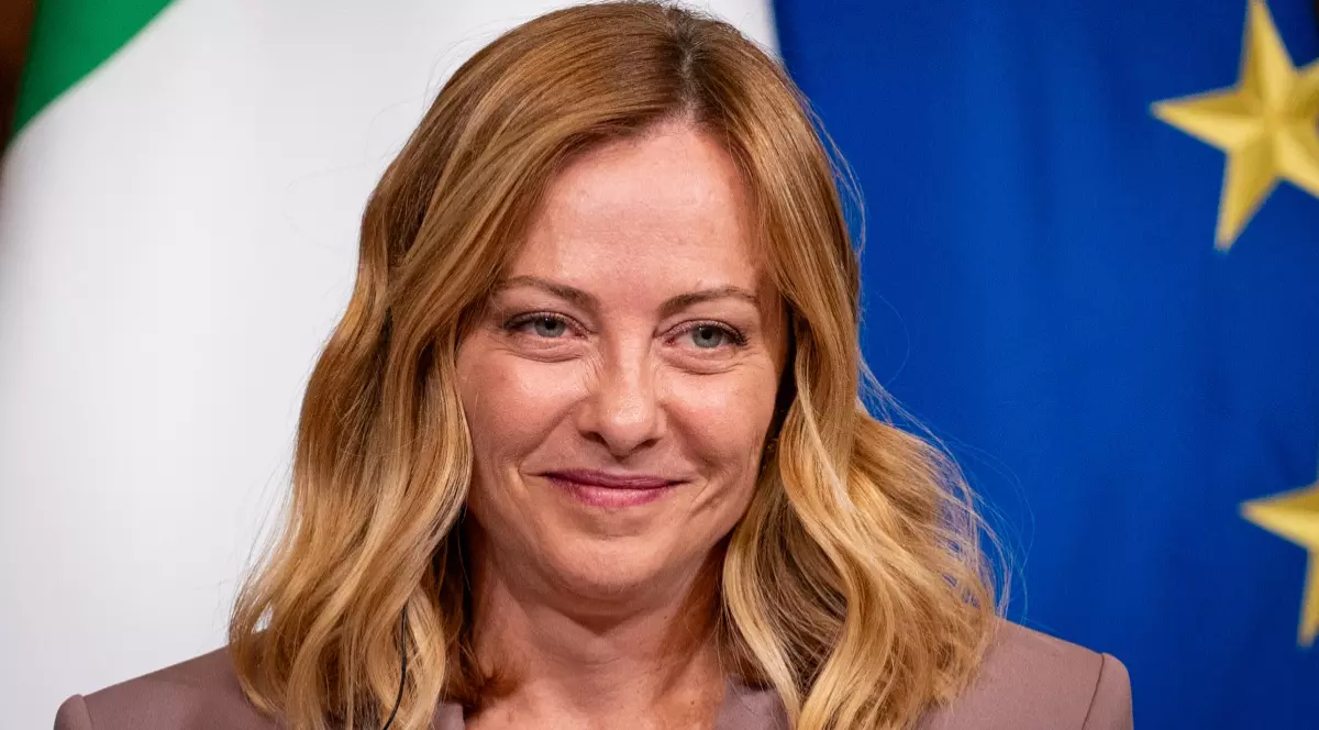 În imagine este ilustrată Giorgia Meloni, îmbrăcată într-un sacou roz.