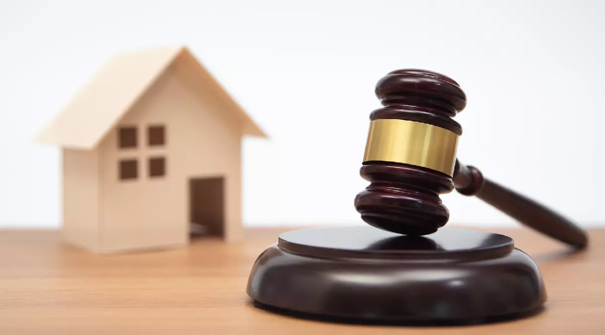 Casă miniaturală pe masă de lemn și ciocan de judecător