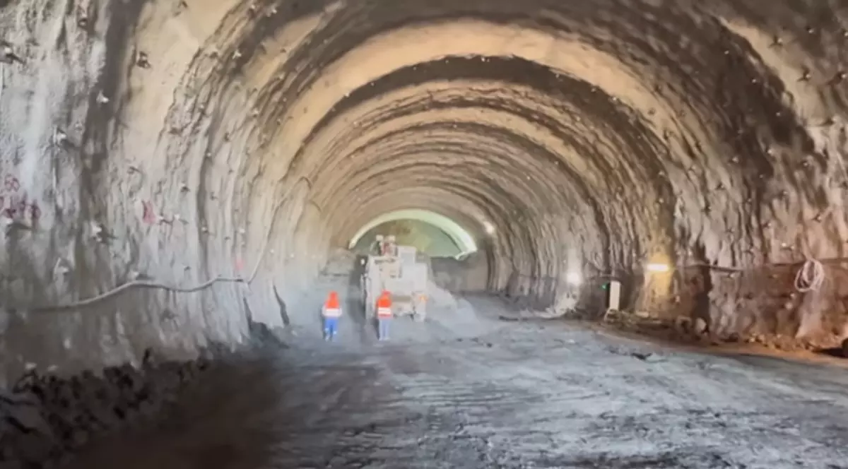 Imaginea prezintă interiorul unui tunel aflat în construcție. În partea centrală a imaginii se observă doi muncitori care poartă veste reflectorizante portocalii.