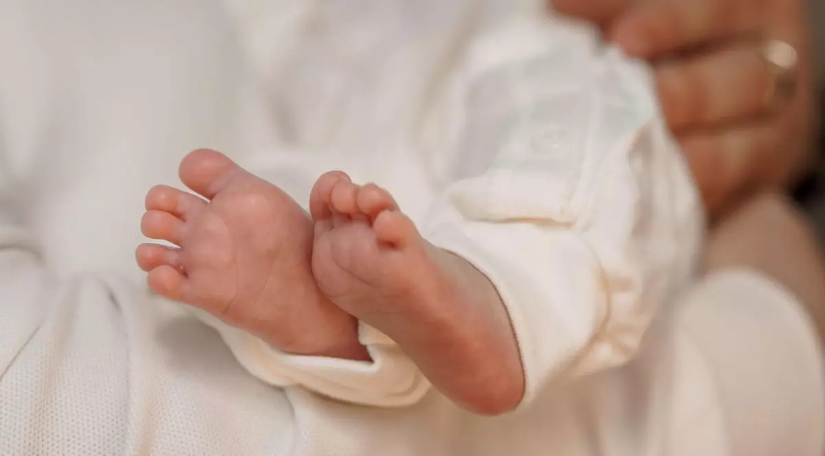 Prim-plan cu piciorușe de nou-născut ținute ușor în mâini iubitoare, înfășurate într-o pânză albă moale