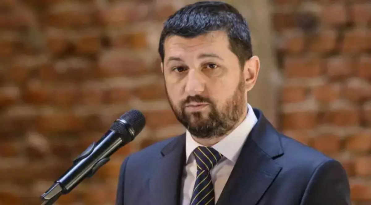 În imagine este ilustrat Marius Lulea, îmbrăcat în costum negru, poartă o cămașă albă și o cravată. Acesta se află în fața unui microfon.