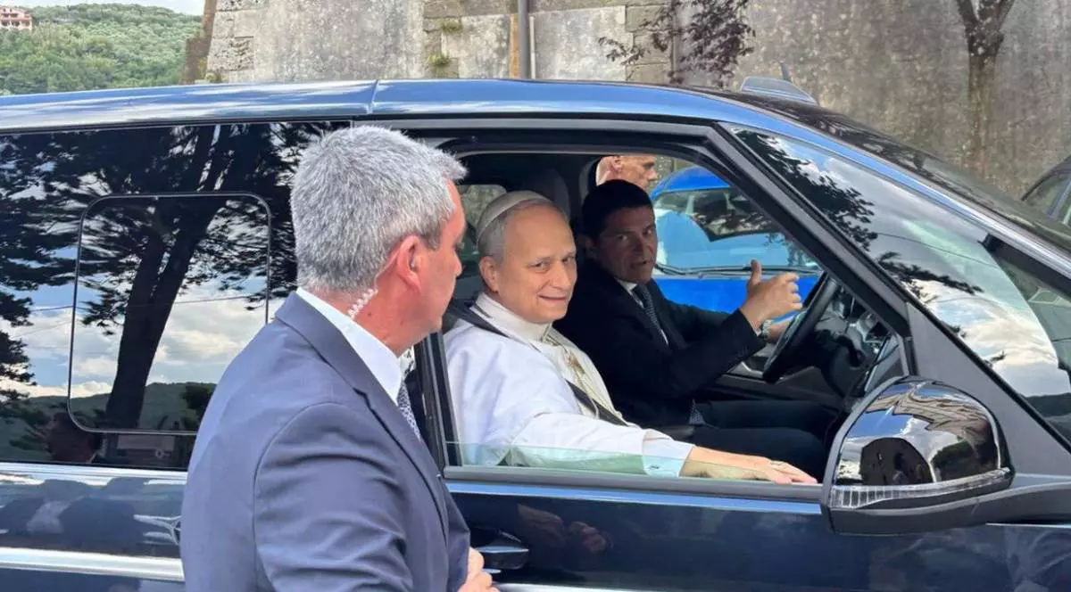 Papa Leon al XIV-lea așezat pe locul din dreapta-față al unei mașini Volkswagen Multivan, în timp ce este escortat de un șofer și personal de securitate.