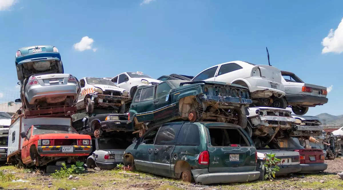 Parc auto de dezmembrări, unde mai multe mașini vechi sunt stivuite în grămezi, majoritatea deteriorate.