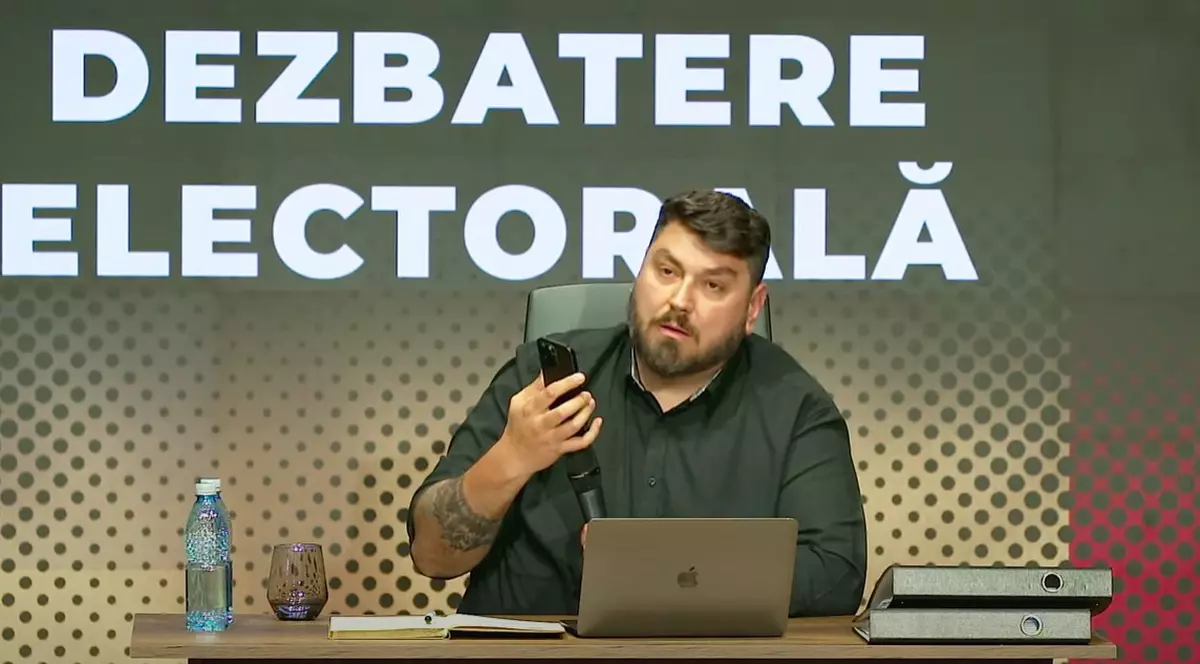 Micutzu alais Cosmin Nedelcu, in studio, la birou, cu un telefon in mana si un laptop in fata