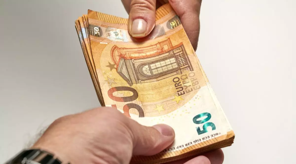 Mâna unui bărbat care ține mai multe bancnote de 50 de euro și le îndreaptă spre o femeie care a pus mâna pe ele