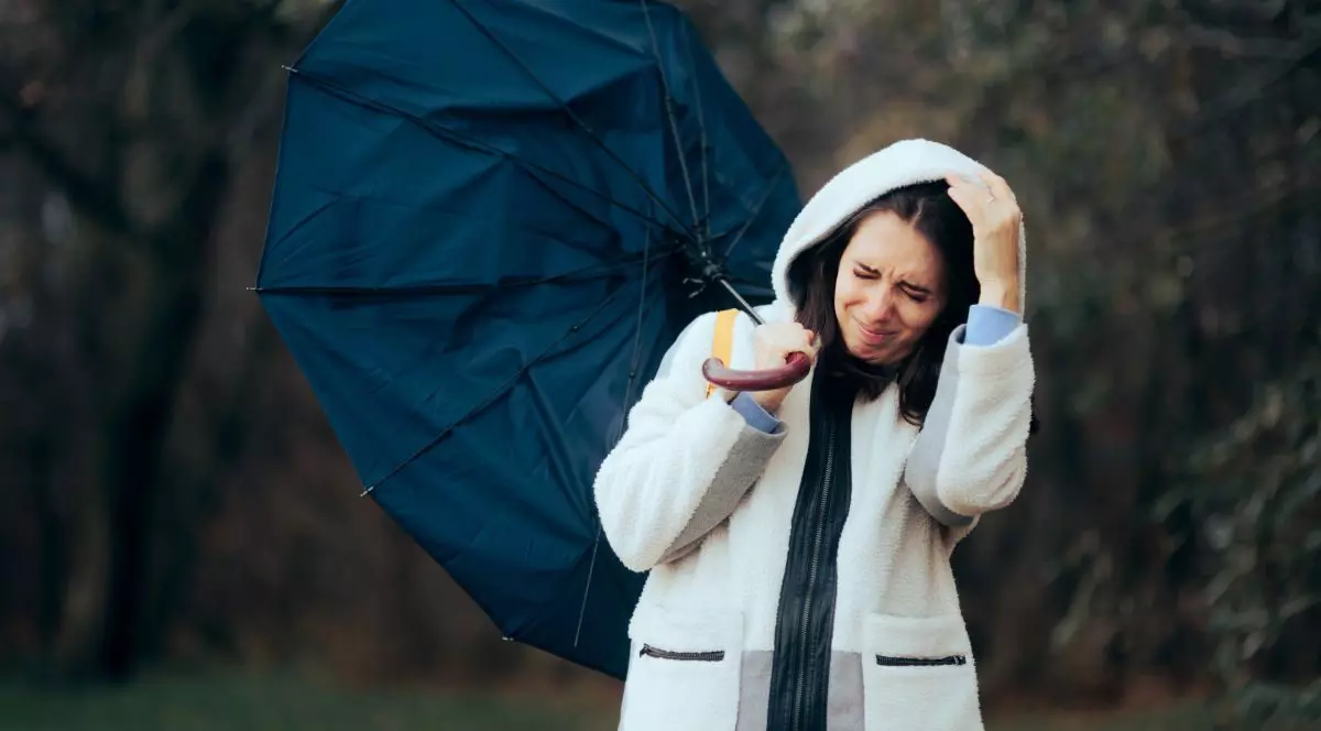 O femeie îmbrăcată în alb și cu glugă pe cap încearcă să își țină umbrela deschisă în timpul unei furtuni