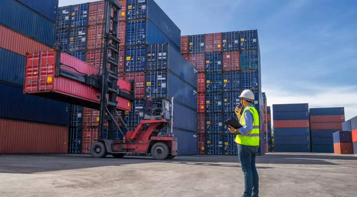 Un angajat cu vestă reflectorizantă, în timp ce se ocupă de așezarea containerelor ce transportă produse din China, într-un port