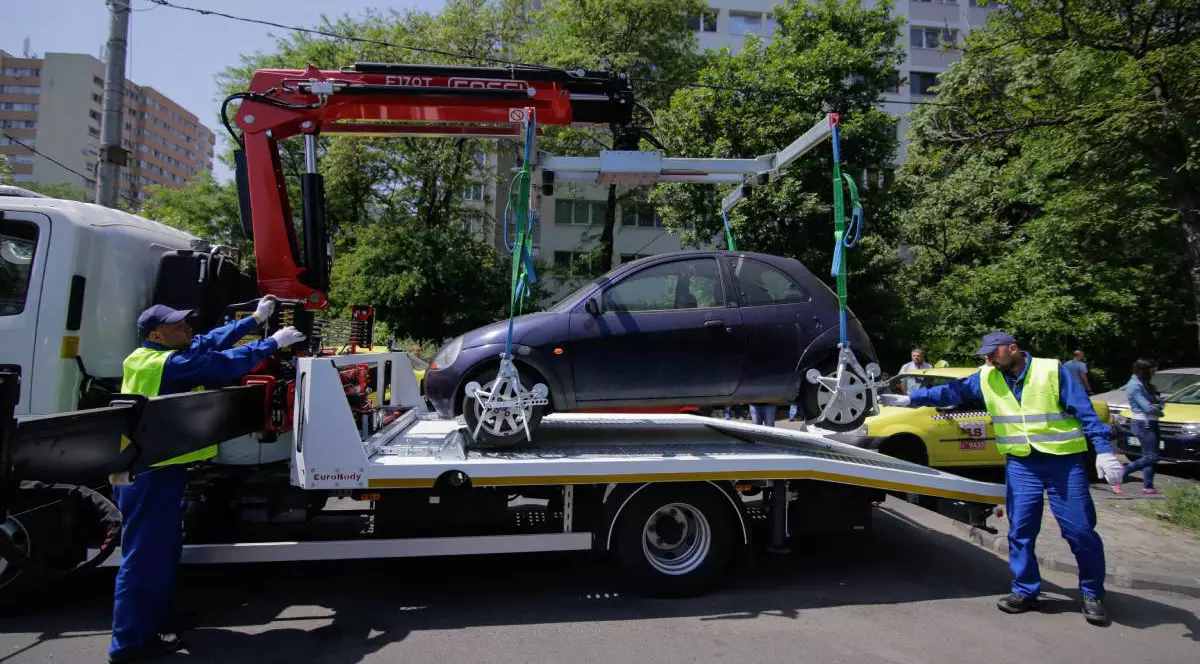 Ridicare a unei mașini parcat ilegal în București. În imagine apar doi angajați îmbrăcați în uniforme reflectorizante