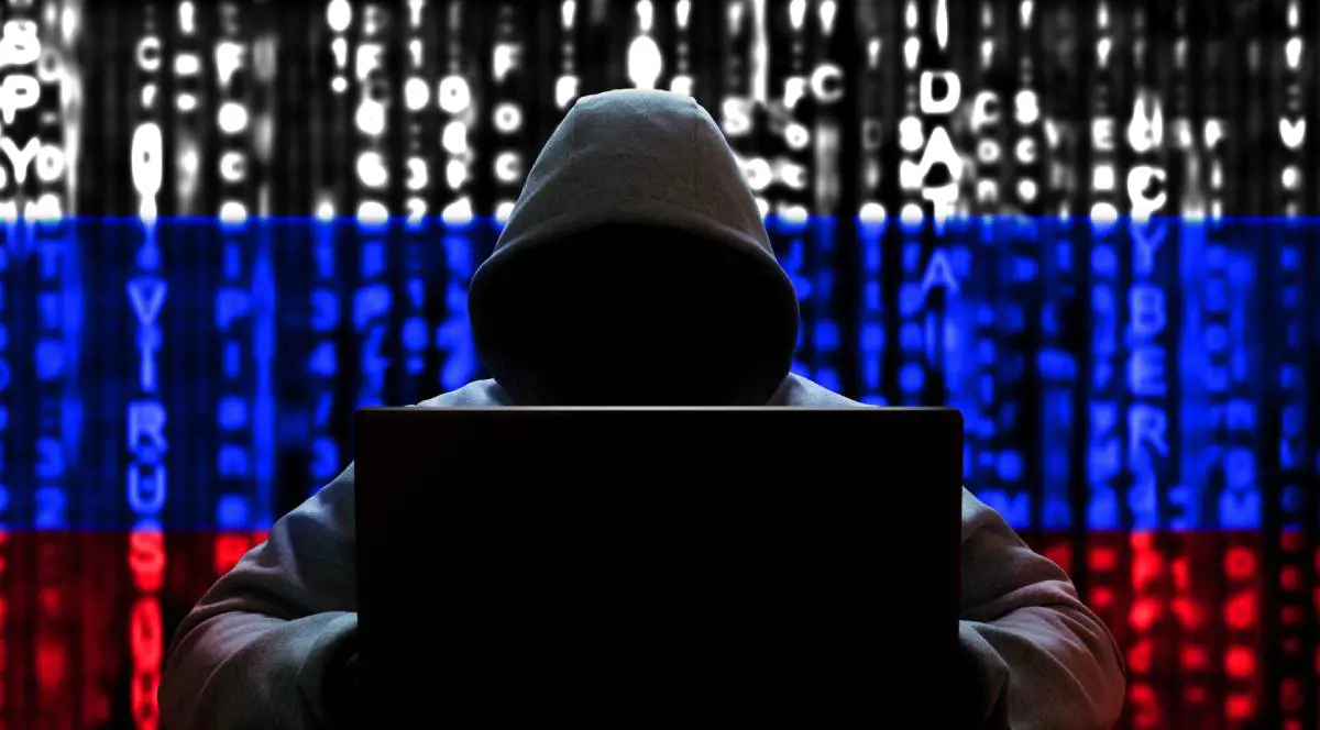 Un spion hacker îmbrăcat în hanorac și cu laptopul în brațe în timp ce pe fundal se vede steagul Rusiei.