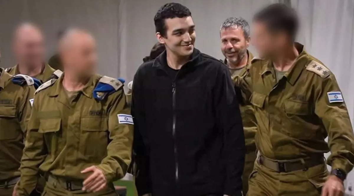 Tânărul israeliano-american, îmbrăcat sport, in hanorac si pantolon negre. încpnjurat de soldați în uniforme kaki eliberat de Hamas
