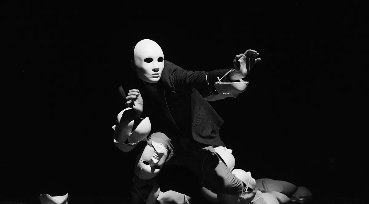 Un barbat in intuneric cu multe masti in jur si pe fata