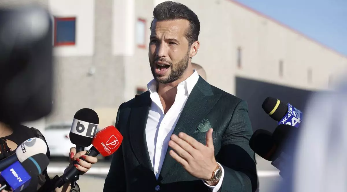 Tristan Tate, îmbrăcat la costum, răspunde la întrebările jurnaliștilor, în fața sediului Agenției Naționale de Administrare a Bunurilor Indisponibilizate (ANABI), joi, 2 octombrie 2025, în București, după ce instanța a decis să le inapoieze fraților Tate mașinile confiscate de oamenii legii în 2024
