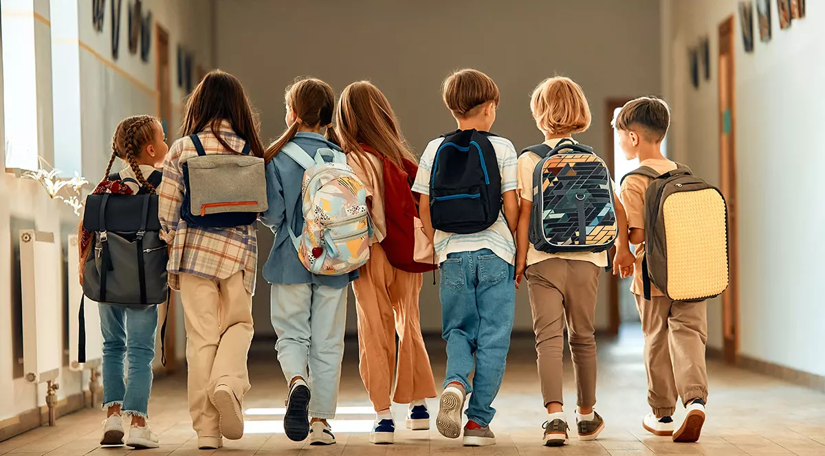 Un grup de școlari cu ghiozdane se plimbă pe coridorul școlii în timpul pauzei.