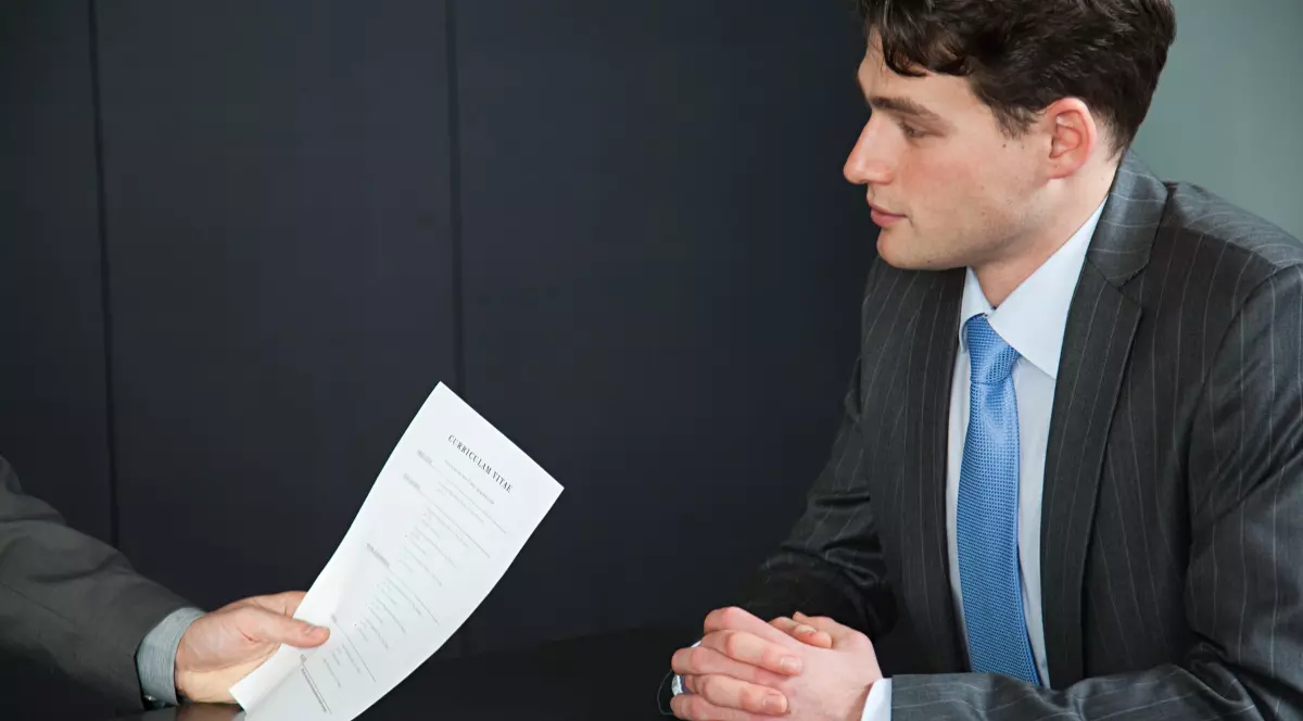 În imagine este ilustrat un tânăr îmbrăcat în sacou, care se află la un interviu pentru job.