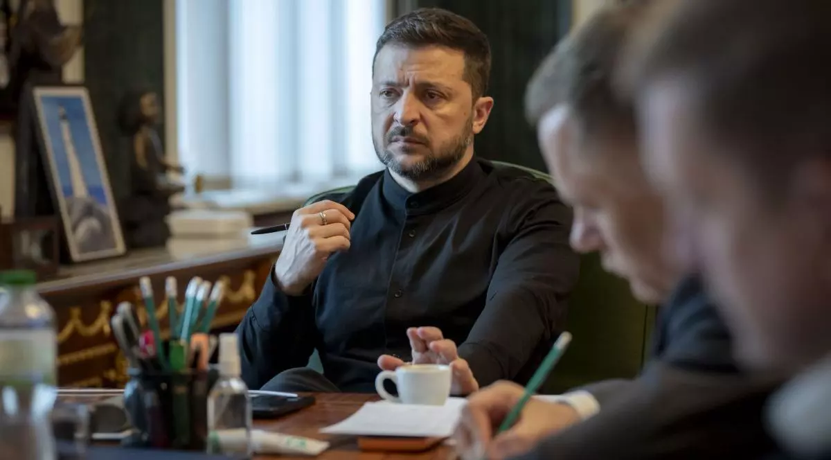 Președintele ucrainean Volodimir Zelenski, îmbrăcat în negru, la birou, alături de câțiva consilieri care scriu