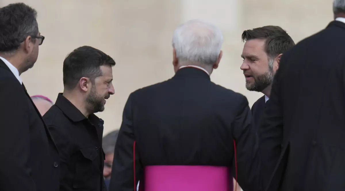 Imaginea surprinde un moment de dialog între mai multe persoane aflate într-un cadru oficial. În stânga este Volodimir Zelenski, iar în partea dreaptă este JD Vance.