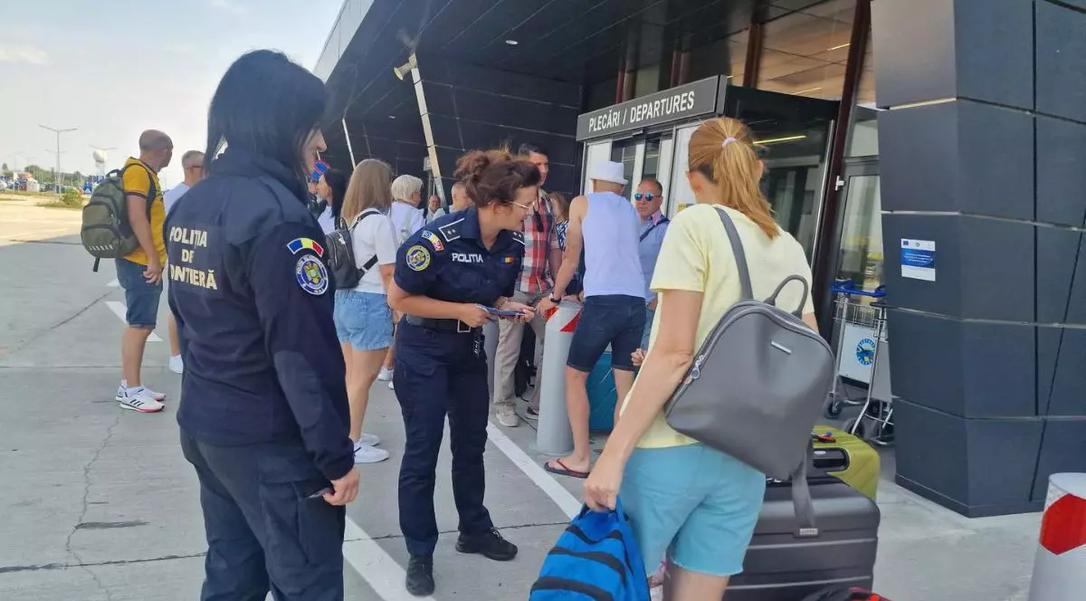 Două polițiste discută cu mai mulți oameni care cară bagaje în fața unei intrări marcate cu textul „Plecări/ Departures” a Aeroportului Internațional Oradea, 17 iunie 2025