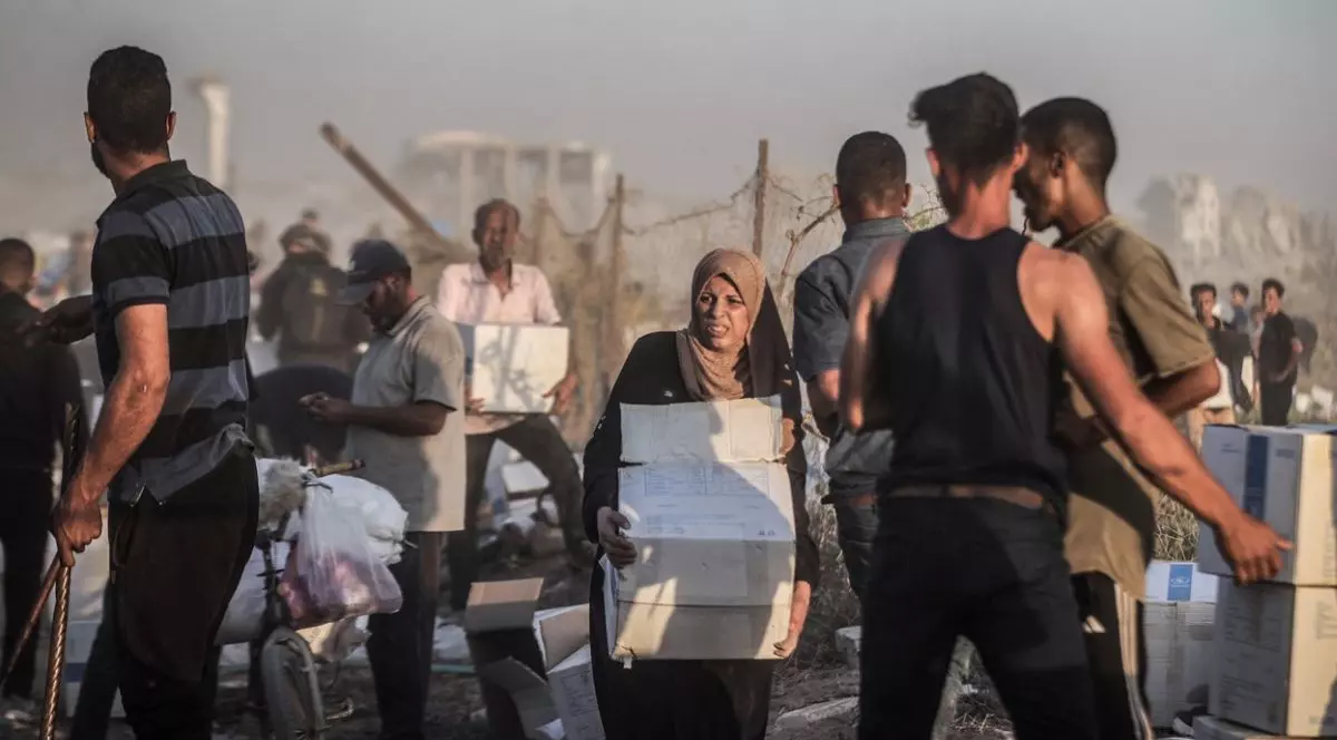 In imagine femei și bărbați palestinieni cară cutii și saci cu ajutoare umanitare,