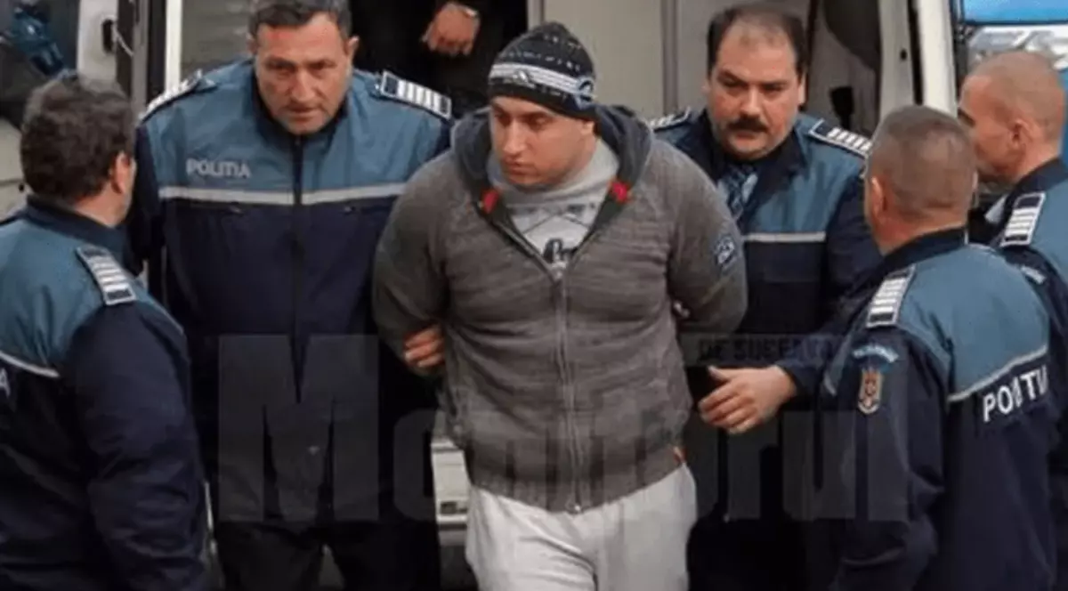 Alexandru Huțuleac este escortat de mai mulți polițiști. Acesta poartă un hanorac gri, pantaloni sport albi și o căciulă