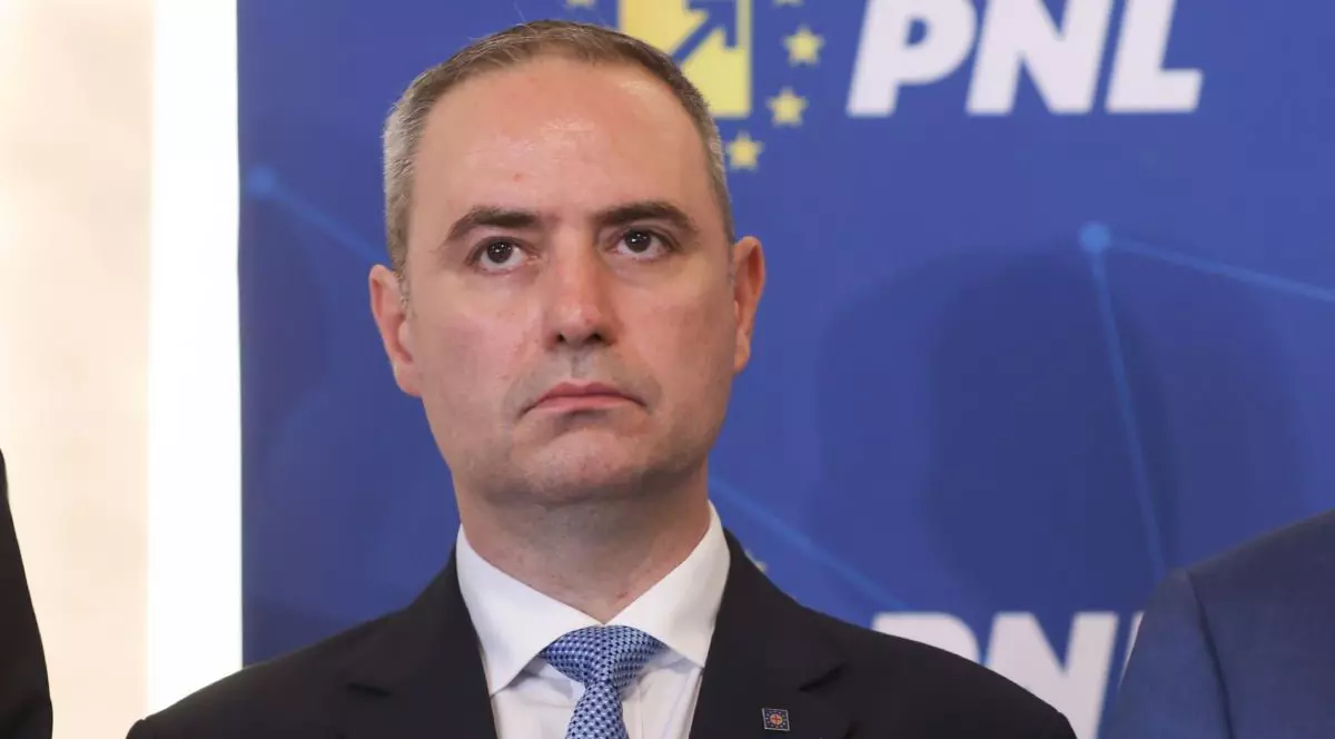 Prim plan Alexandru Nazare în timplul unor declaratii, 22 iunie 2025, cu panou albastru cu galben in spate, pe care se vede sigla PNL