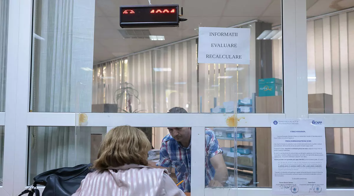 O femeie stă la ghișeu să obțină informații de la angajatul instituției