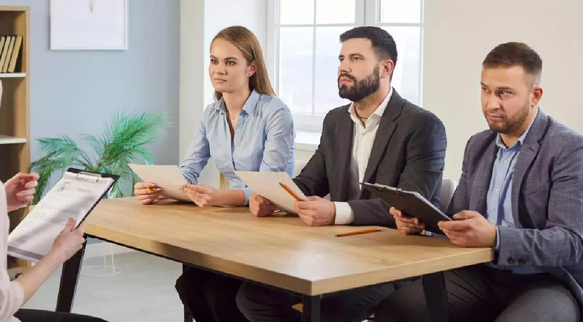 Angajatorul vorbește cu angajații la interviul de angajare stând la masa de conferințe, discutând despre experiența profesională