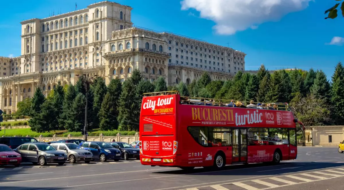 Un autobuz turistic roșu în București, plimbând turiștii în fața Palatului Parlamentului
