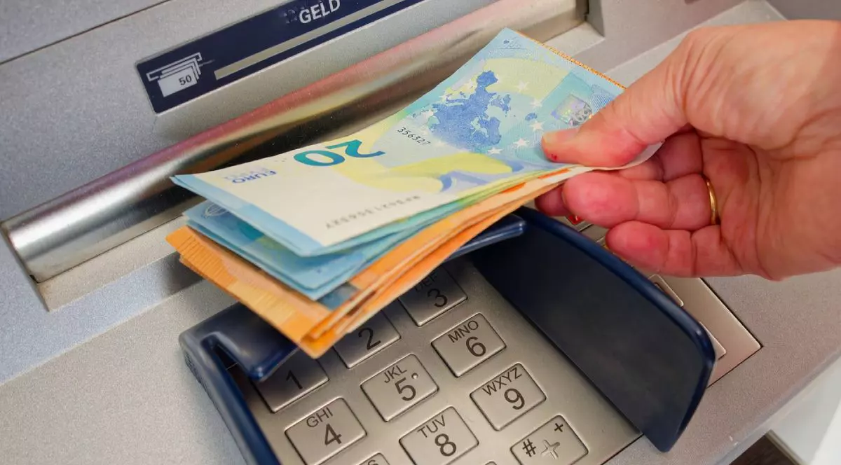 Bancnote de euro, de 20 și 50 de euro, ținute într-o mână, în fanta de retragere a unui bancomat