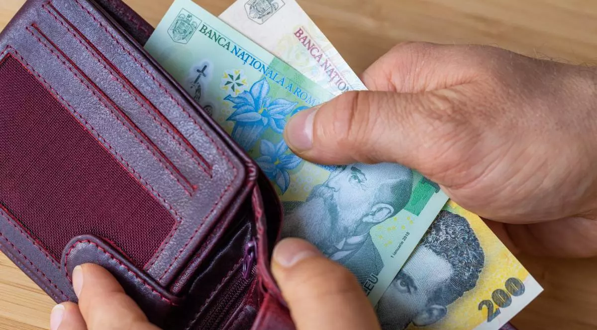 O persoană în vârstă în timp ce scoate hârtii de un leu și 50 de lei dintr-un portofel vișiniu