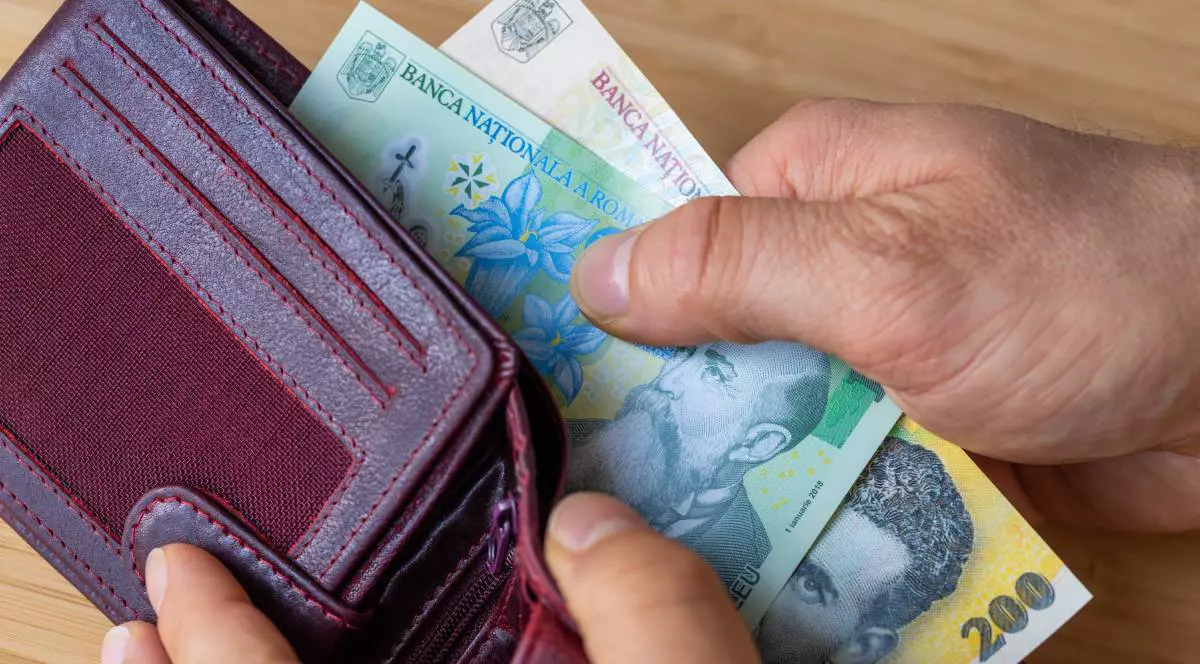 O persoană în vârstă în timp ce scoate hârtii de un leu și 50 de lei dintr-un portofel vișiniu