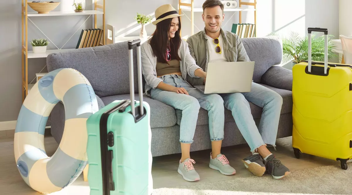 Imagine cu doi tineri, bărbat (dreapta) și femeie (stânga) stând pe canapea cu un laptop în brațe. În stânga se află un colac de salvare și o valiză turcoaz, iar în dreapta un geamantan galben. Tânăra poartă o pălărie crem cu o bandă neagră, blugi bleu, un hanorc gri și un top verde. Bărbatul poartă blugi bleu, o bluză albă și o jachetă verde