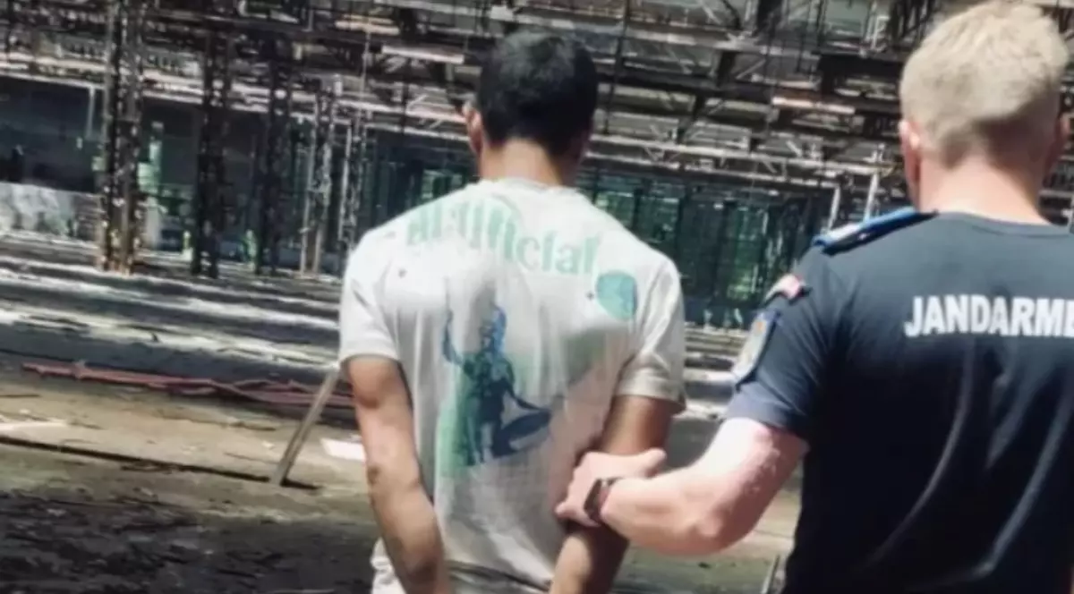 Un bărbat încătușat este ținut de un jandarm la o hală de pe platforma Rulmentul din Brașov