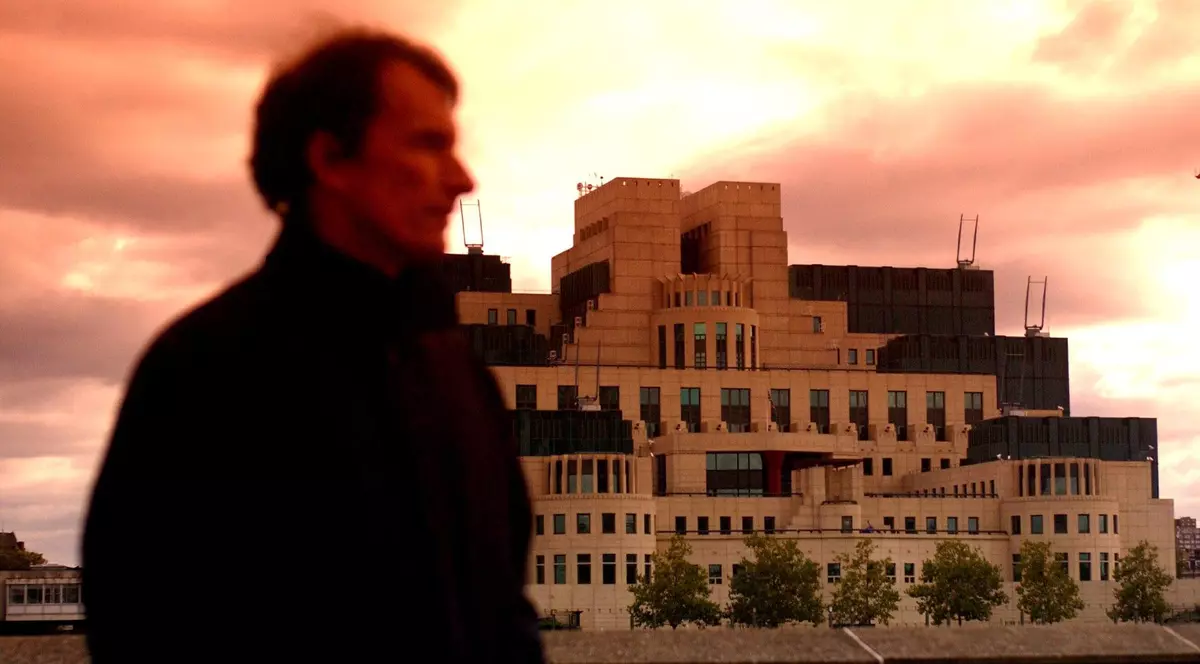 Poză cu un bărbat care poartă un palton negru în fața sediului MI6 din Londra