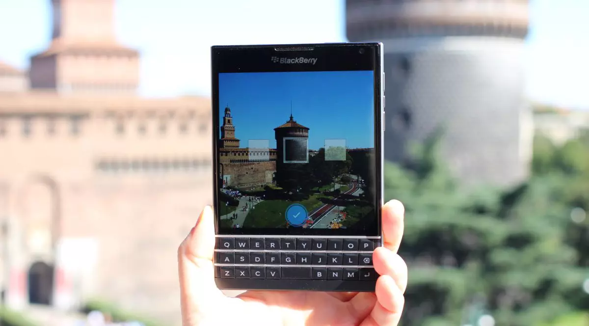 Un telefon BlackBerry Passport, ținut în mână de o persoană în fața unui castel din Italia.