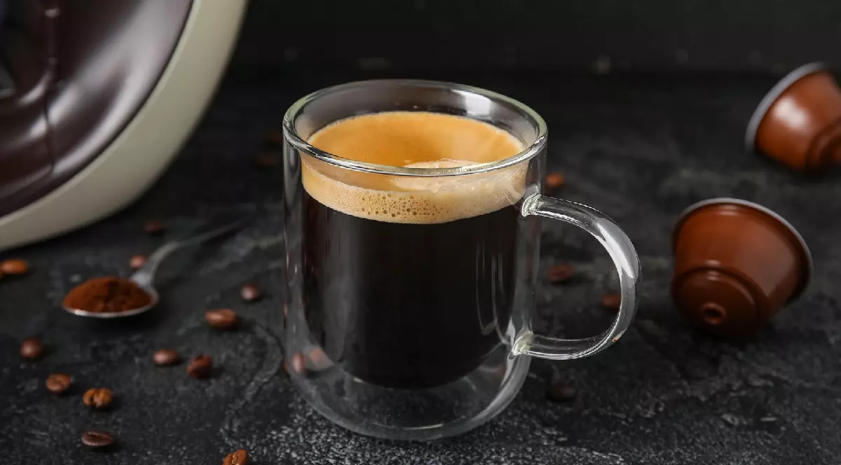 o cană cu cafea neagra și două capsule de cafea
