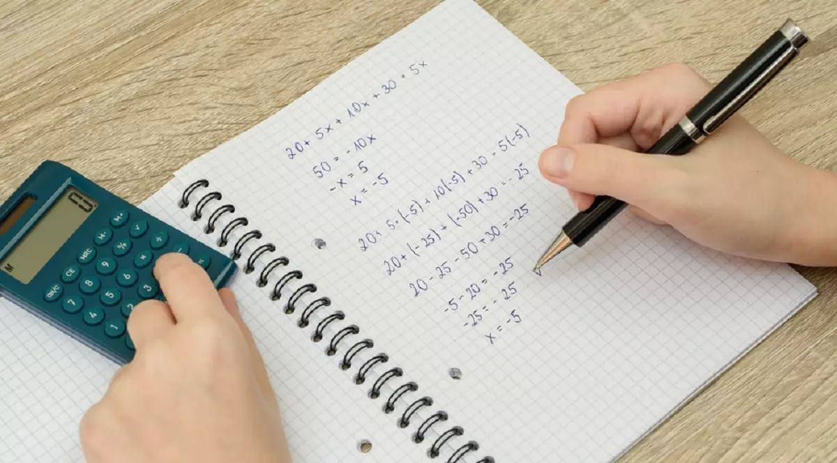 Ce este şi cum se determină cel mai mare divizor comun - Imagine cu o pagină de caiet de matematică cu calcule şi un calculator de birou alături