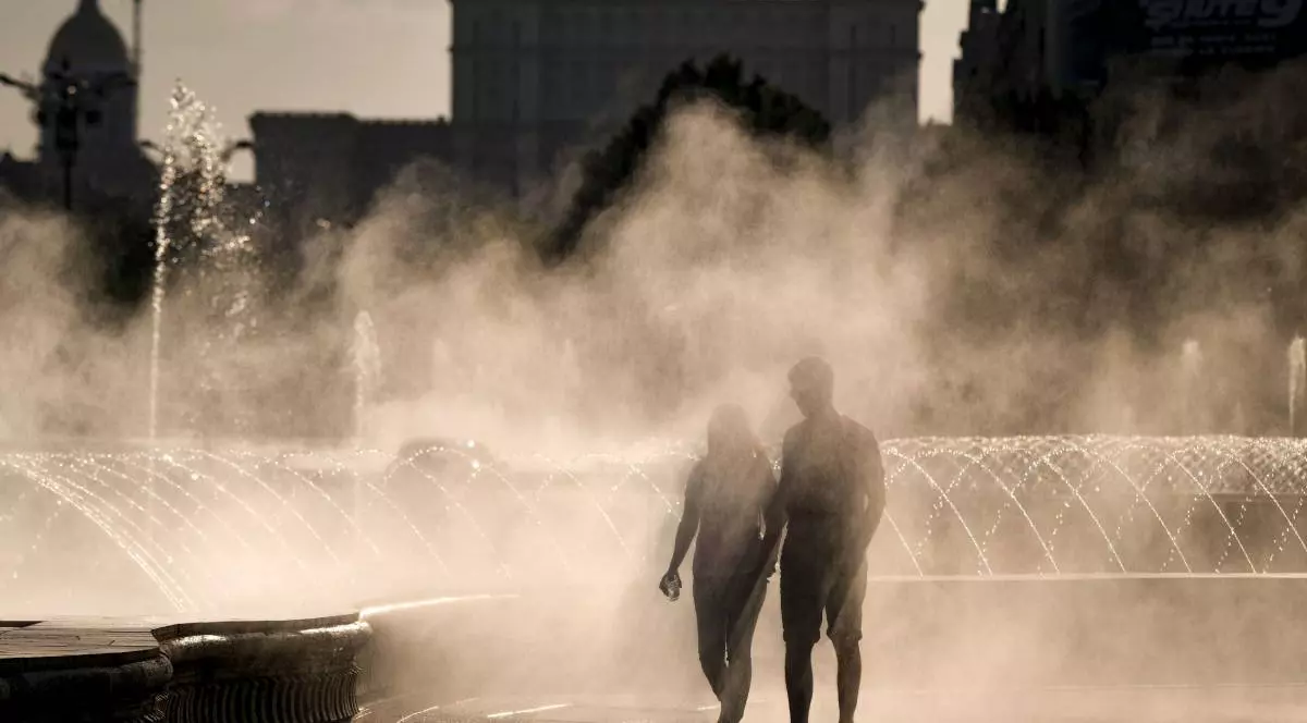 Două persoane care încearcă să se ferească de canicula din București stând în dreptul unei fântâni, în timp ce arde soarele.