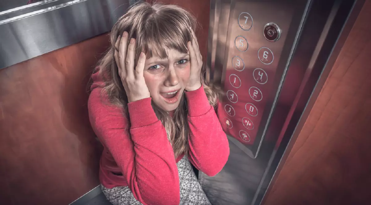 Ce înseamnă când visezi lift - O femeie, cu o bluză roșie, își ține mîinile pe cap, părând îngrozită de faptul că este blocată într-un lift