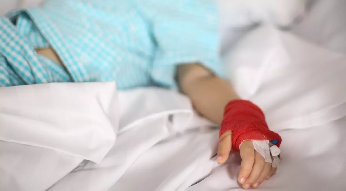 o canulă pe mâna unei fetițe bolnave, care stă pe un pat, într-un spital