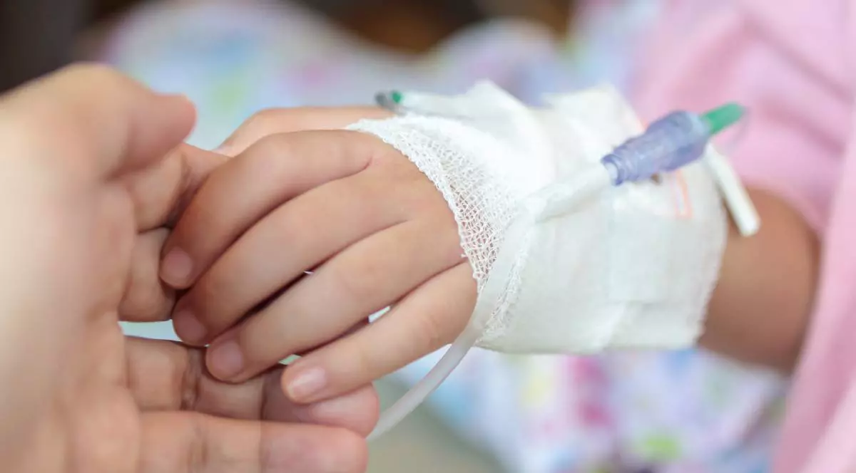 Un copil internat în spital cu o branulă în mână, în timp ce mama îl ține de mână