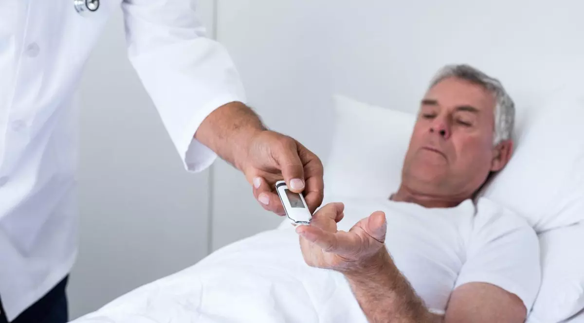 Unui bărbat îi este măsurat nivelul de glucoză din sânge, stând pe un pat din spital.