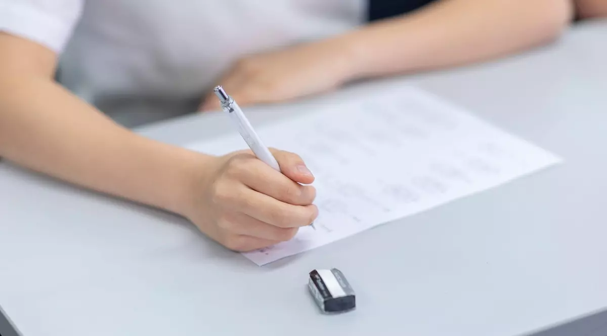 Imagine cu un elev în bancă în timpul unui examen. Ține un pix în mână