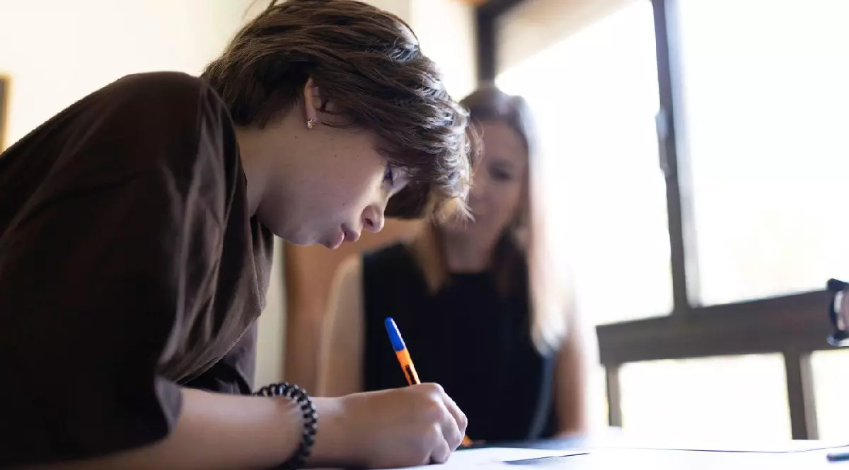 Elev care se concentrează asupra testului, scriind pe hârtie, cu ajutorul profesorului