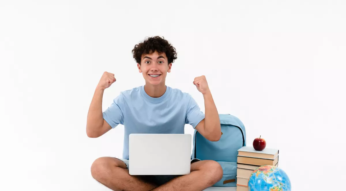 Elev fericit cu un laptop în brațe și lângă mai multe cărți