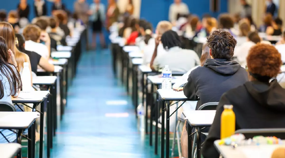 Mai mulți elevi de liceu stau în bănci de o persoană, așezați pe două rânduri