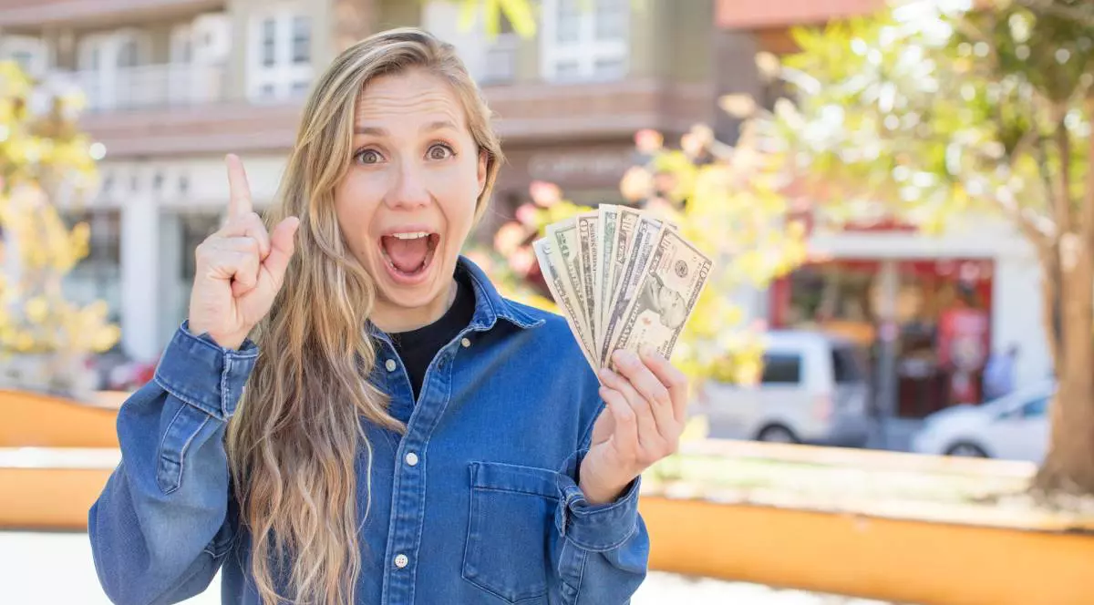 O femeie blondă ține mai multe hârtie de dolari în mână și zâmbește după ce a câștigat un premiu