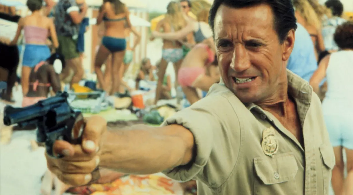 O scenă din filmul „Jaws” în care un bărbat ține mâna în care are un pistol întinsă în fața sa